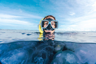 A woman in a black wetsuit is in the water with jellyfish. the jellyfish are floating around her