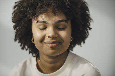 Smiling young woman with eyes closed against white wall