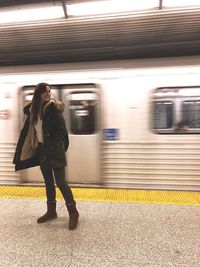Young woman standing on platform against moving subway train