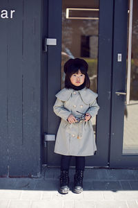 Korean girl in a gray coat and cap and round glasses stands the street in spring at the glass doors