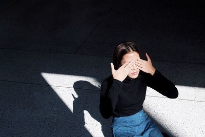 High angle view of young woman covering eyes with hands while sitting outdoors