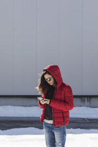 Young woman using phone on snow covered footpath