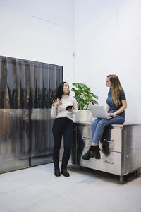 Female bloggers talking while using technologies in creative office