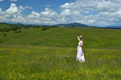 Woman showing with her hand towards hills and spring sky full of white clouds