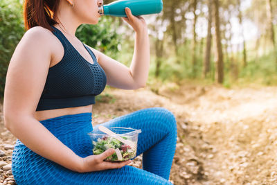 Midsection of woman drinking water in forest