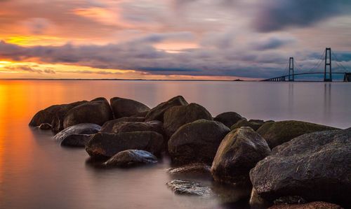 Rocks in sea against sky during sunset