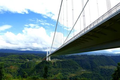 Low angle view of suspension bridge against cloudy sky