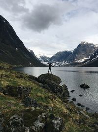 Man standing on rock by sea against sky