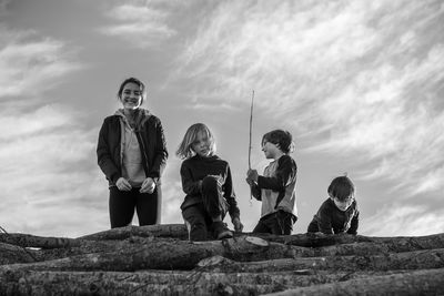 Rear view of children on logs against sky