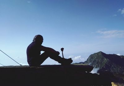 Silhouette man sitting on cliff against sky