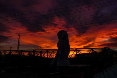 Silhouette man standing by railing against orange sky