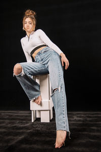 Portrait of woman sitting against black background