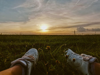 Low section of person on field against sky during sunset