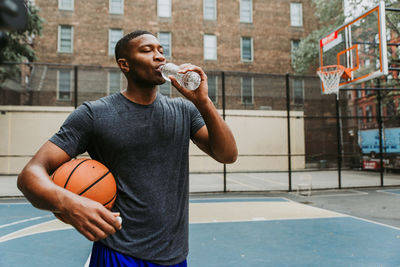 Full length of young man holding basketball in city