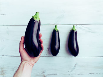 Cropped hand of man holding eggplant over table
