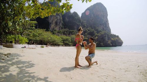 Full length of shirtless man proposing woman at beach