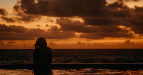 Silhouette woman looking at sea against sunset sky