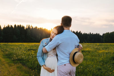 Rear view of couple on field against sky during sunset