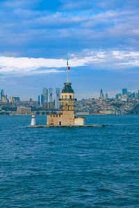 Buildings in sea against cloudy sky