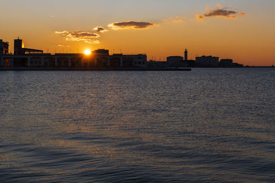 Sea by buildings against sky during sunset