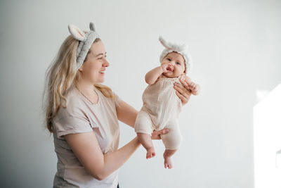 Mom blonde and newborn daughter in white with rabbit ears photo on a light background