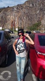 Young woman wearing sunglasses standing on car