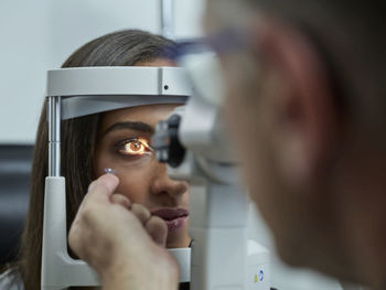 Optometrist examining young woman's eye, contact lens on index finger