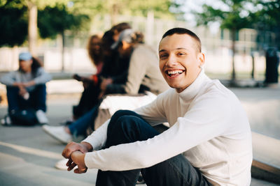 Portrait of happy young man sitting with friends at skateboard park