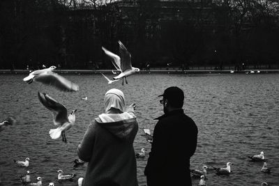 Rear view of man with seagulls flying over lake