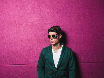 Portrait of young man standing against pink wall