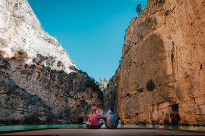 People sitting on rock formation against sky