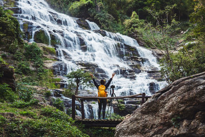 Rear view of woman with camera enjoying waterfall view in forest