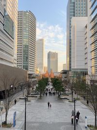 People on street amidst buildings in city against sky