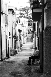 Man sitting on alley amidst buildings in city