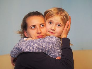 Portrait of mother and daughter embracing against wall at home