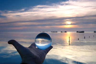 Person holding sea against sky during sunset