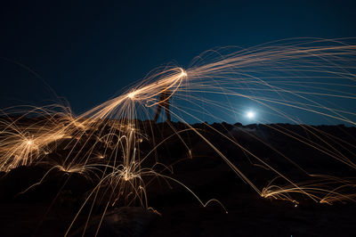 Man making wire wool at beach against clear sky at night