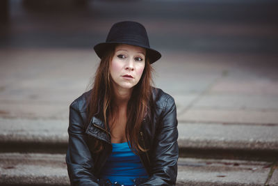 Woman wearing hat and leather jacket sitting in city