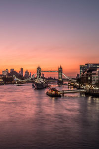 Illuminated city by river during sunset