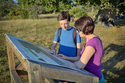 Mother and son reading signboard on field