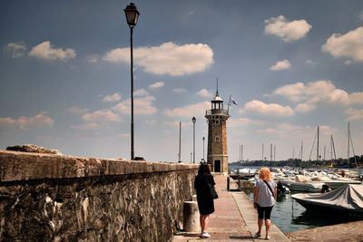 Two women with a lighthouse and a sky behind and boats