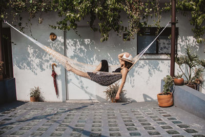 Woman relaxing in hammock against wall at yard