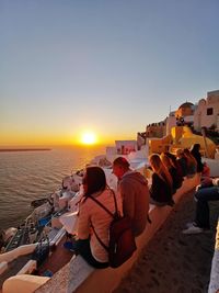 People sitting on beach by sea against sky during sunset