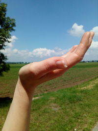 Midsection of person hand on field against sky