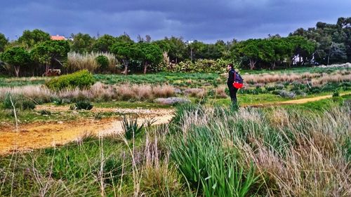 Side view of young man standing on grassy field against cloudy sky