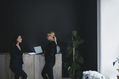 Female colleagues discussing while standing by cabinet in home office