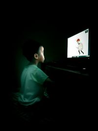 Rear view of a boy sitting at dark room