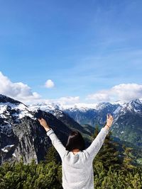 Rear view of woman standing with arms raised on snow covered mountain