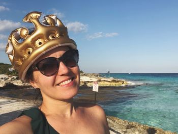 Portrait of young woman wearing inflatable crown at beach against sky