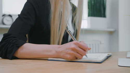 Midsection of woman holding pen over book on table